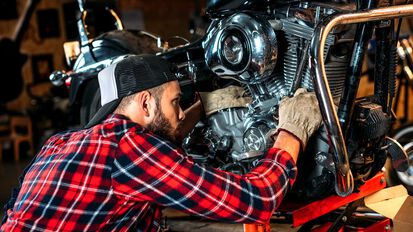 Mann in kariertem Hemd und Baseballcap bei der Wartung eines Motorrads in einer Werkstatt zur Vorberitung zum überwintern.